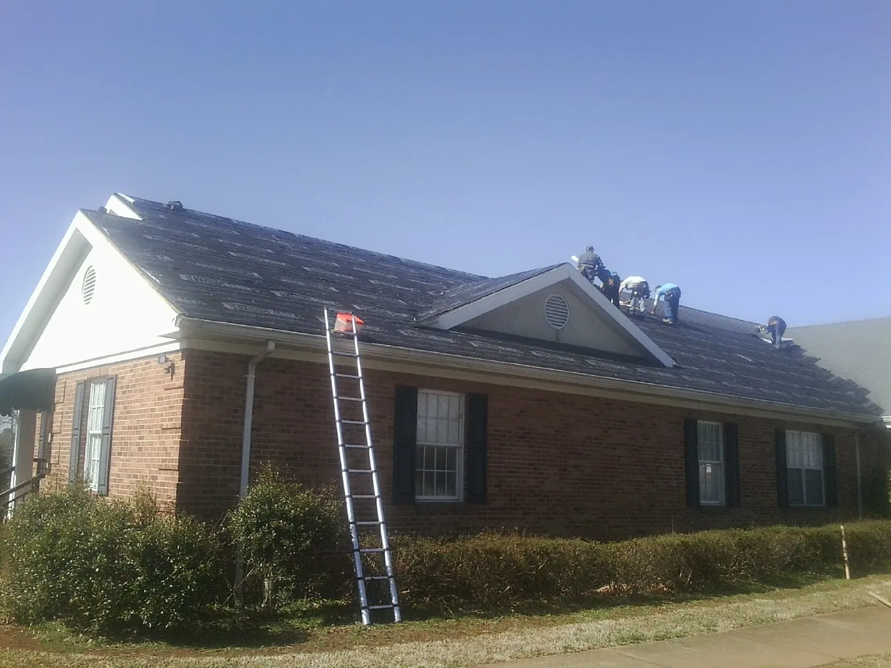 Crew tearing shingles off a brick ranch roof with a ladder set — Emergency Roof Repair work by our crew in Gardiner