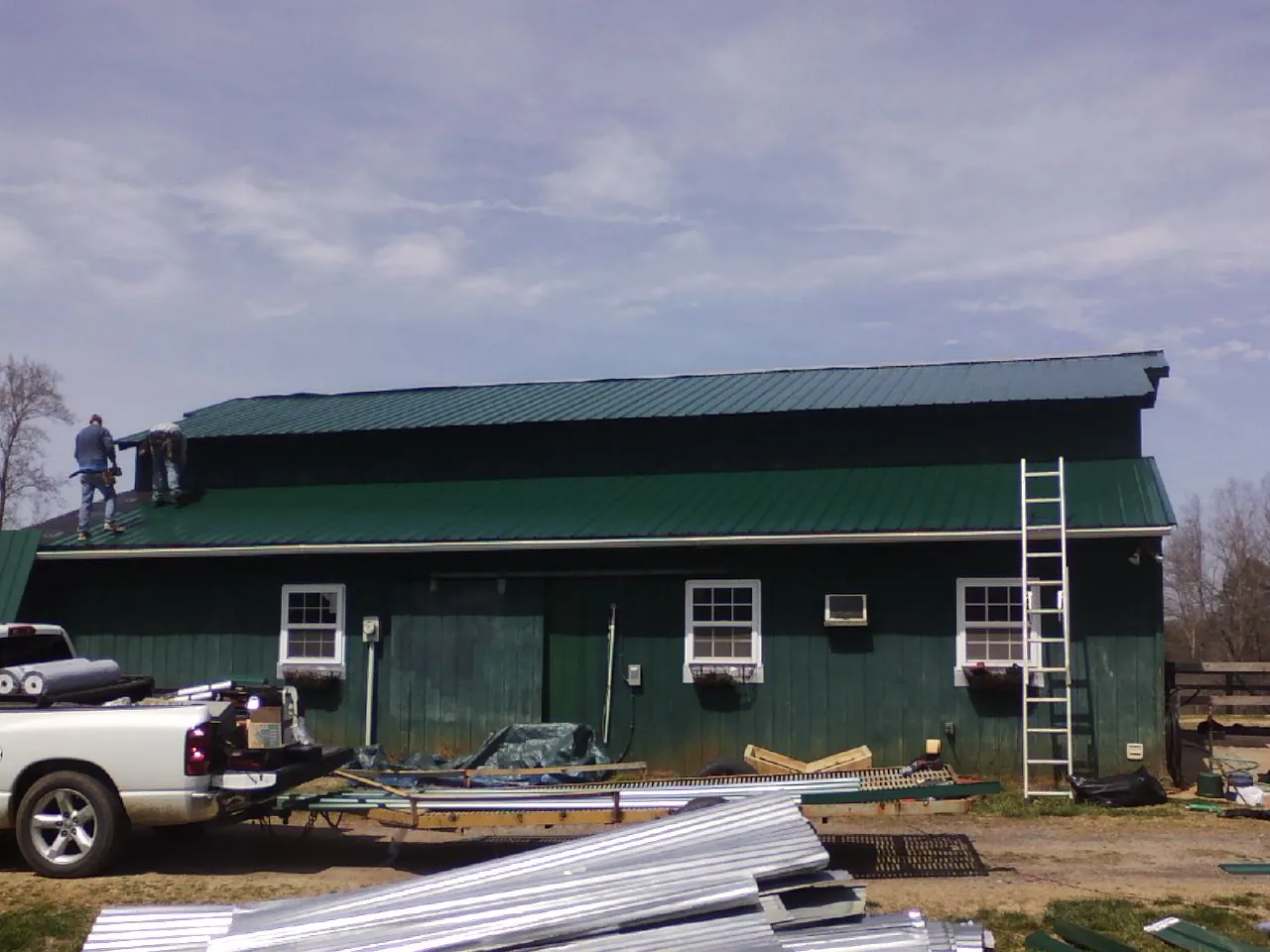 Crew installing green metal roofing on a large green barn in Gardiner