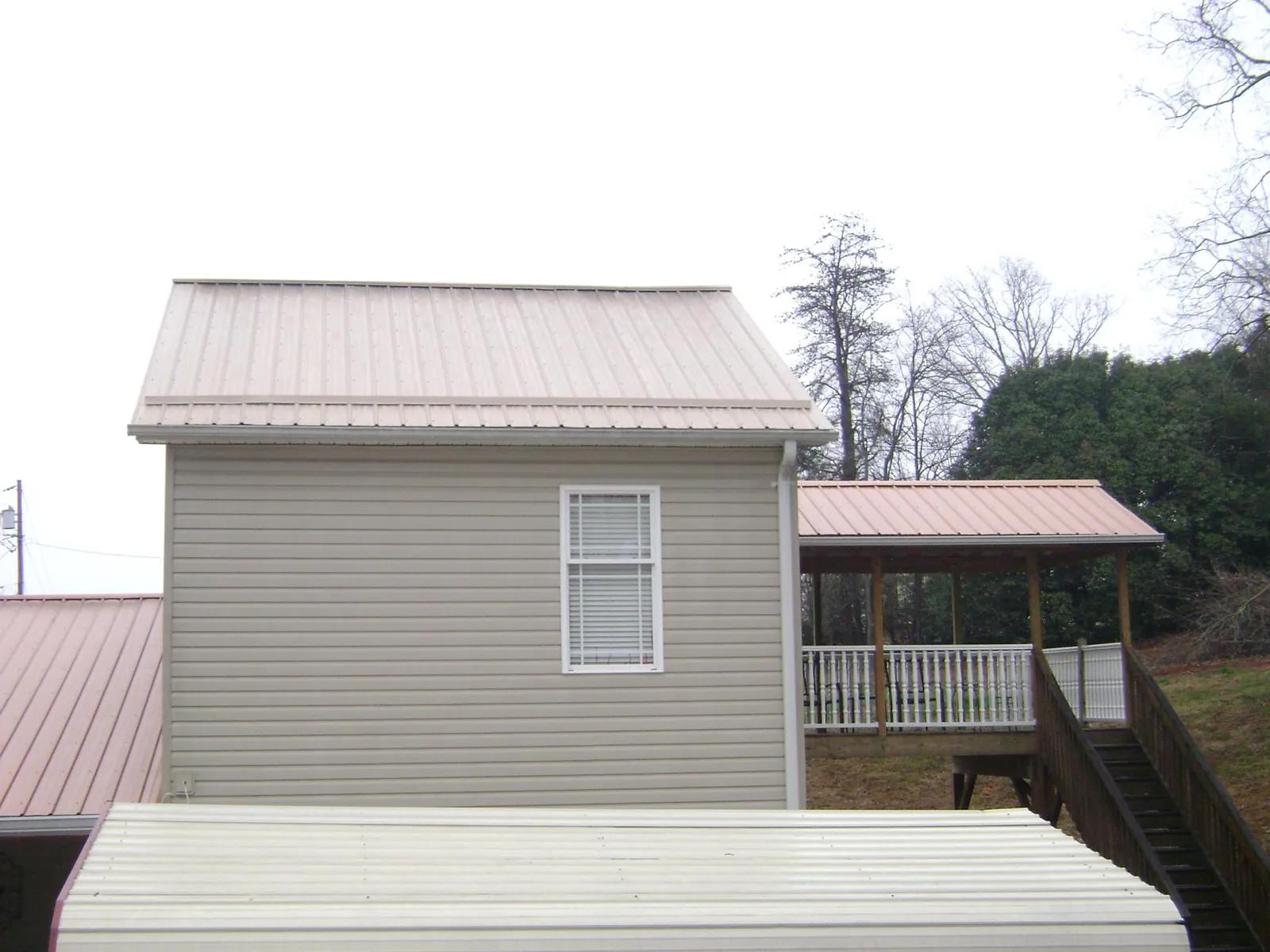 Tan metal roofs on a two story addition and attached porch, from a Roof Replacement job in Gardiner
